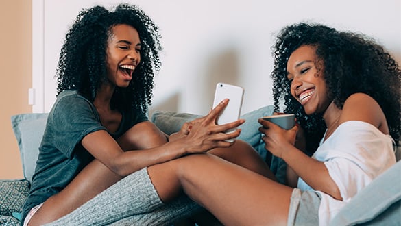 happy women sitting on couch looking at a phone
